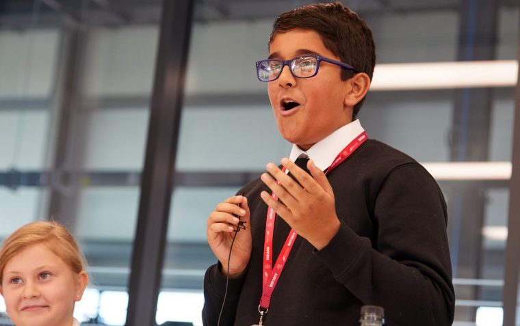 A young pupil passionately sharing his ideas while his team mate smiles and listens to him