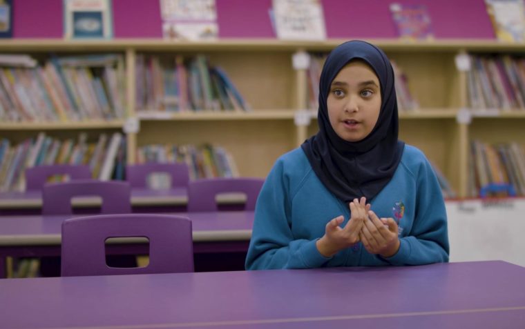 A pupil expressing her ideas with a lot of books in the background