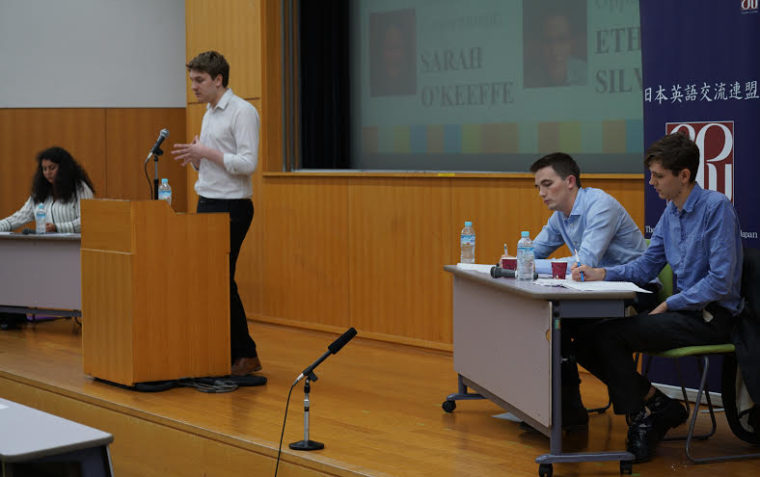 A person speaking from the podium and the other team listening to the arguments
