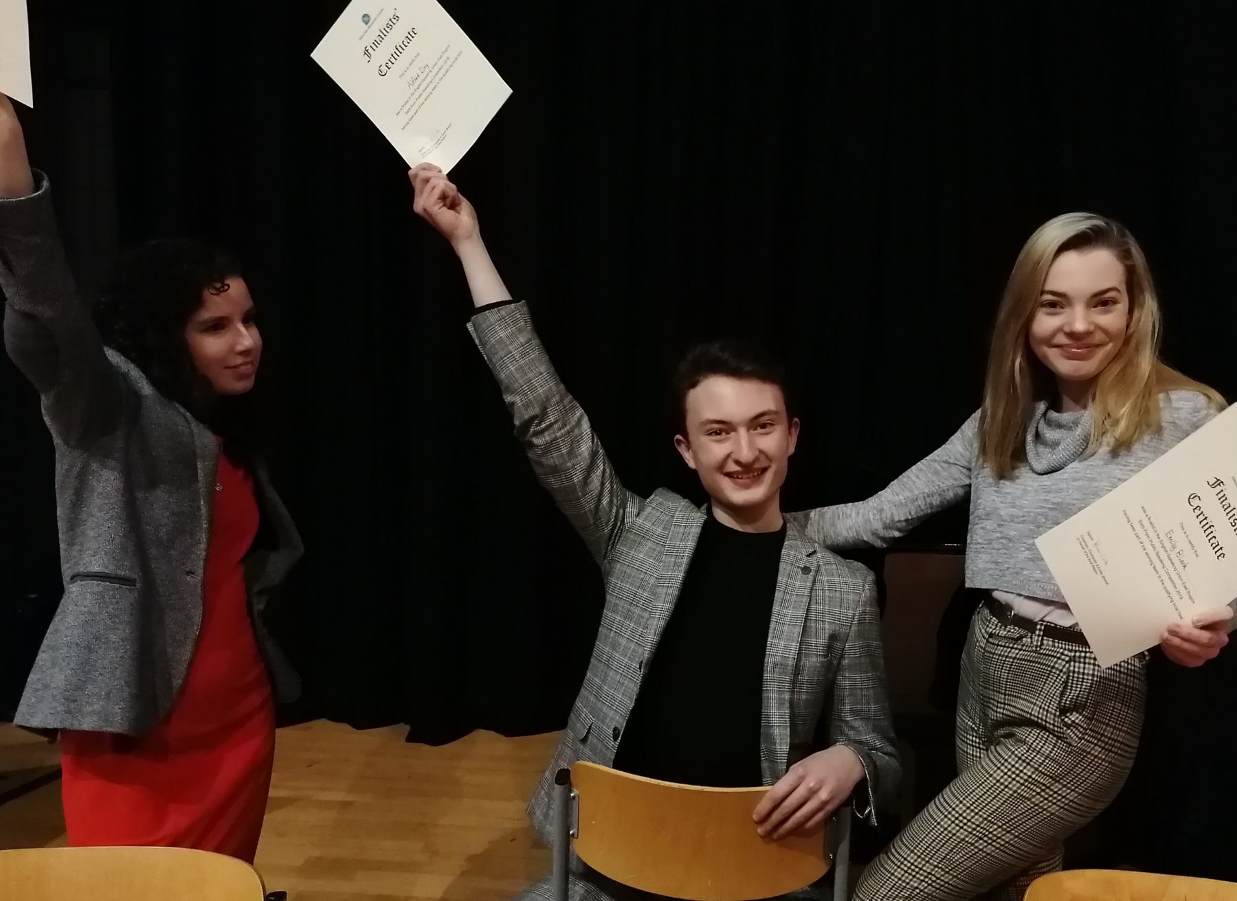 3 students, one boy on a chair and two girls standing, posing with their finalist certificate