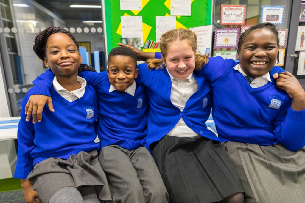 Team shot of primary school children (three girls and a boy) smiling with linked shoulders