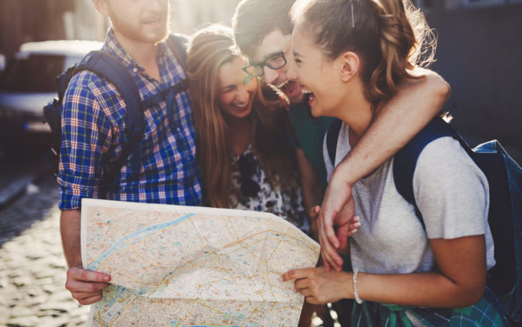 Three secondary school students standing close together in a group hug smiling and holding a paper map together.