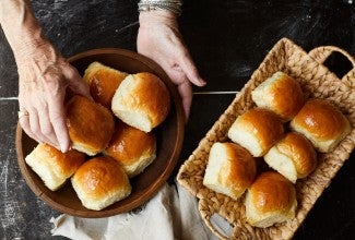 A baker putting soft white dinner rolls into a bread basket