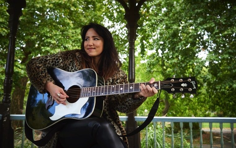 Image of KT posing with a guitar in a park