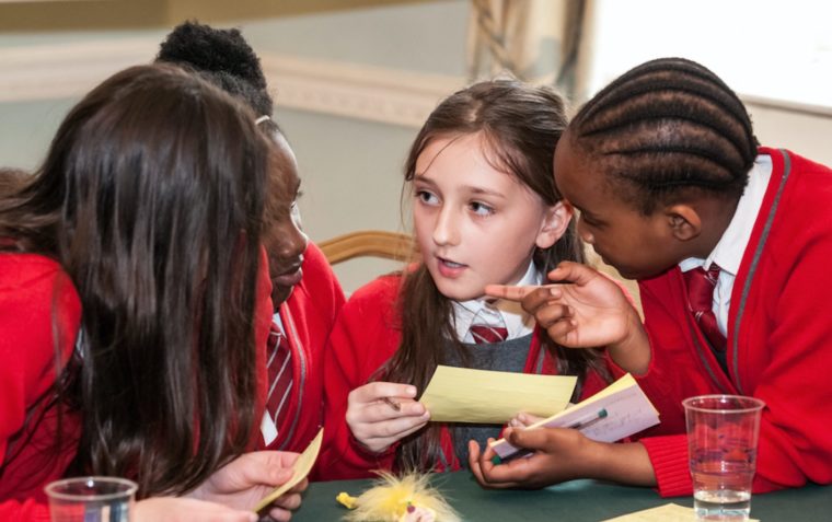 A group of primary school pupils (a boy and three girls) sitting around a table and playing debating games for students