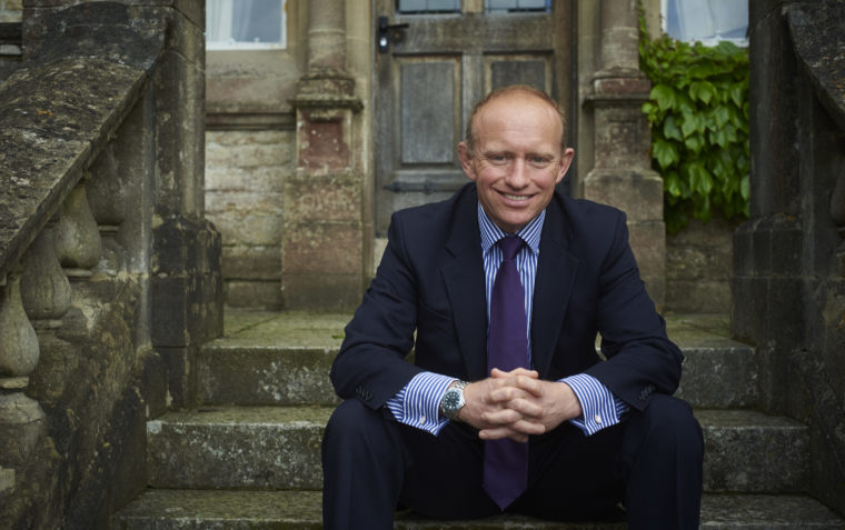 A photograph of Mark Mortimer sitting on the stairs in front of an old building.