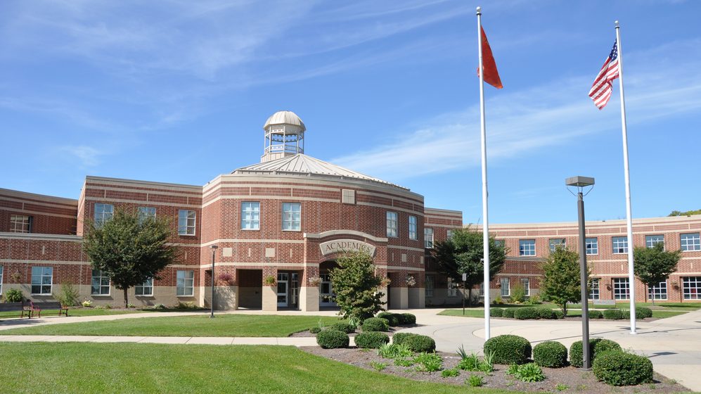 A photo of the main entrance of Academia school building with the flags of the United States of America and China.