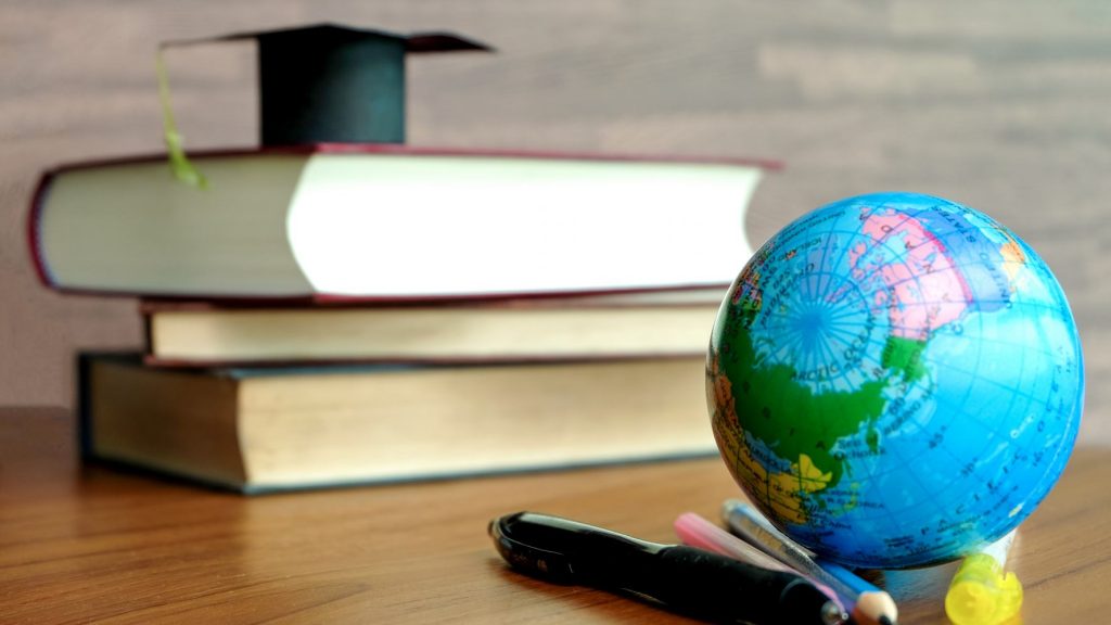 A staple of three books with a coronation hat on top of them on one end of the the table and a globe with a mixture of crayons and markers on the end of the table.