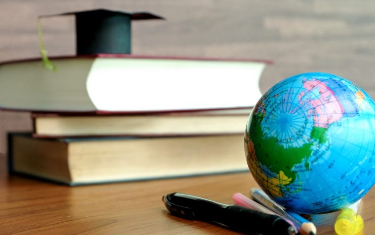 A staple of three books with a coronation hat on top symbolising scholarship on one end of the table, while a globe with a mixture of crayons and markers sits on the other end.